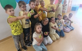 Grupa dzieci w zielonych koszulkach z gruszkami pozuje pod ścianą z namalowanymi drzewami&nbsp;