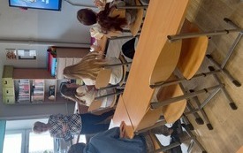Uczniowie siedzą w ławkach i słuchają wypowiedzi kobiety