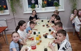 Uczniowie siedzą przy stole w jadalni i jedzą pizzę
