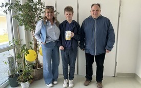 Nauczyciel, pracownik hospicjum i uczeń pozują do zdjęcia. Uczeń trzyma puszkę z pieniędzmi