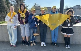 Sześcioro uczni&oacute;w stoi przy murku, trzymają ż&oacute;łtą chustę i puszkę na pieniądze