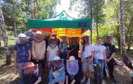 Zdjęcie grupowe uczni&oacute;w w strojach pszczelarza podczas wizyty w pasiecie