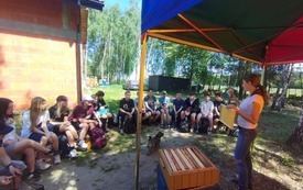Zdjęcie uczni&oacute;w podczas zajęć warsztatowych w pasiece pszczeli gaj w Rosanowie. Na pierwszym planie pani pszczelarz z ramką, na kt&oacute;rej pszczoły tworzą mi&oacute;d