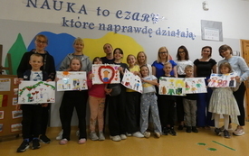 Uczniowie wraz z rodzicami pozują do zdjęcia, trzymają w rękach swoje prace