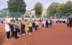 Uczniowie wraz z nauczycielami stoją na boisku szkolnym