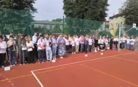 Uczniowie wraz z nauczycielami stoją na boisku szkolnym