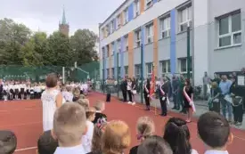 Uczniowie wraz z nauczycielami stoją na boisku szkolnym