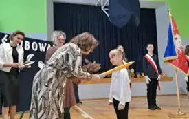 Wicedyrektor szkoły nachyla się nad uczennicą i wygłasza tekst ślubowania