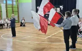 Na zdjęciu uczniowie trzymają flagi narodowe, jeden uczeń wygłasza tekst