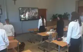 Uczniowie zwr&oacute;ceni twarzą do tablicy, śpiewają hymn