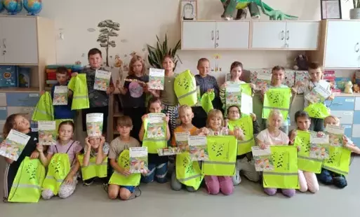 Widać uczniów kl. 2 b, którzy trzymają w rękach dyplomy z napisem "Bezpieczny uczestnik ruchu drogowego". Oprócz dyplomów za pracę na lekcji dzieci otrzymały również worki na buty, lub inne szkolne rzeczy. Trzymają je w rękach. Worki mają fluorescencyjny,