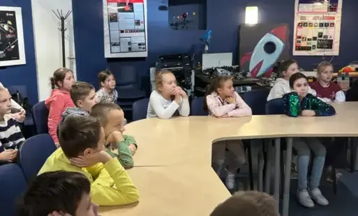 Uczniowie siedzą w planetarium i słuchają prowadzącego