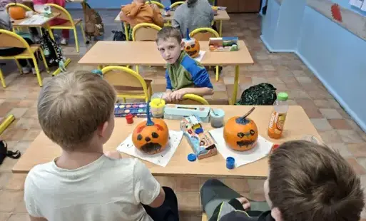 Dwoje uczniów siedzi tyłem do zdjęcia, przed nimi pomalowane dynie, jeden skierowany twarzą do zdjęcia