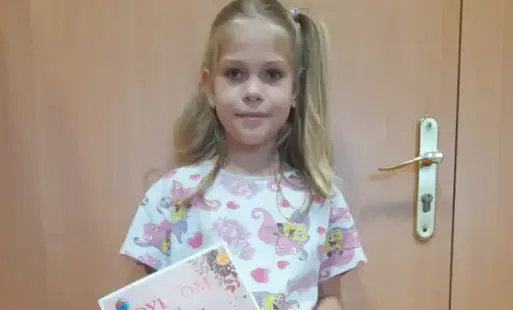 Uczennica trzyma w rękach torbę papierową, z której wystaje dyplom
