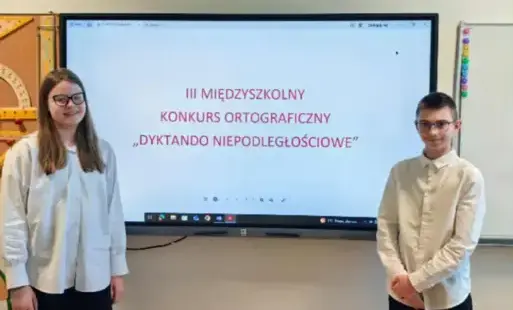 Uczeń i uczennica stoją przy tablicy multimedialnej