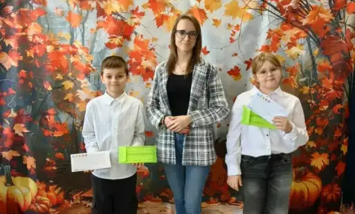 Dwoje uczniów pozuje do zdjęcia z nauczycielką, trzymają w rękach vouchery
