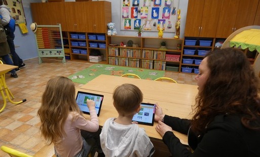 Nauczycielka pokazuje dwojgu dzieci zadanie na tablecie