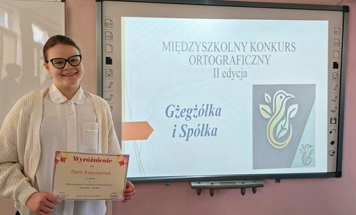Uczennica pozuje z dyplomem przy tablicy multimedialnej