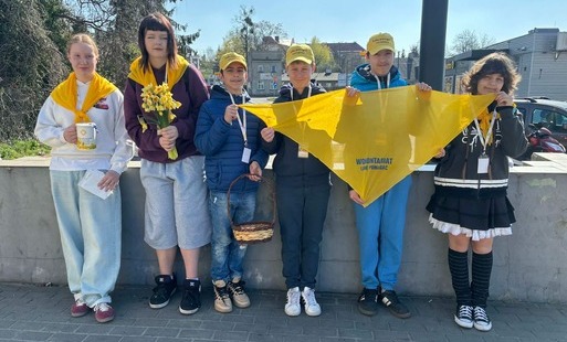 Sześcioro uczniów stoi przy murku, trzymają żółtą chustę i puszkę na pieniądze