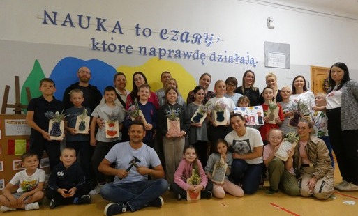 Uczniowie wraz z rodzicami pozują do zdjęcia, trzymają w rękach swoje prace